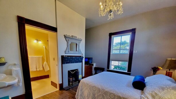 Ein Schlafzimmer mit Bett, Kamin, Fenster mit Blick und einem Badezimmer mit Waschbecken und Toilette.