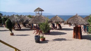 Una playa con sombrillas de paja y sillones de playa, arena suave y una vista despejada del mar.