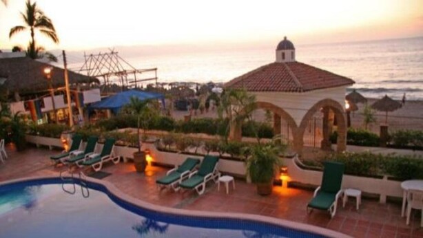 Zona de piscina con sillones reclinables y vistas al océano al atardecer.