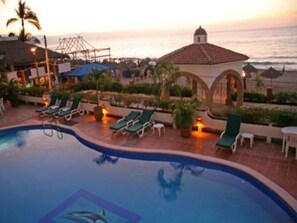A pool area with lounge chairs and a view of the ocean at sunset.
