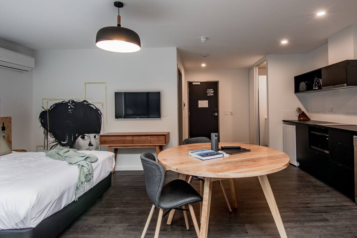 Un dormitorio moderno con cama, mesita de noche y un televisor grande en la pared.