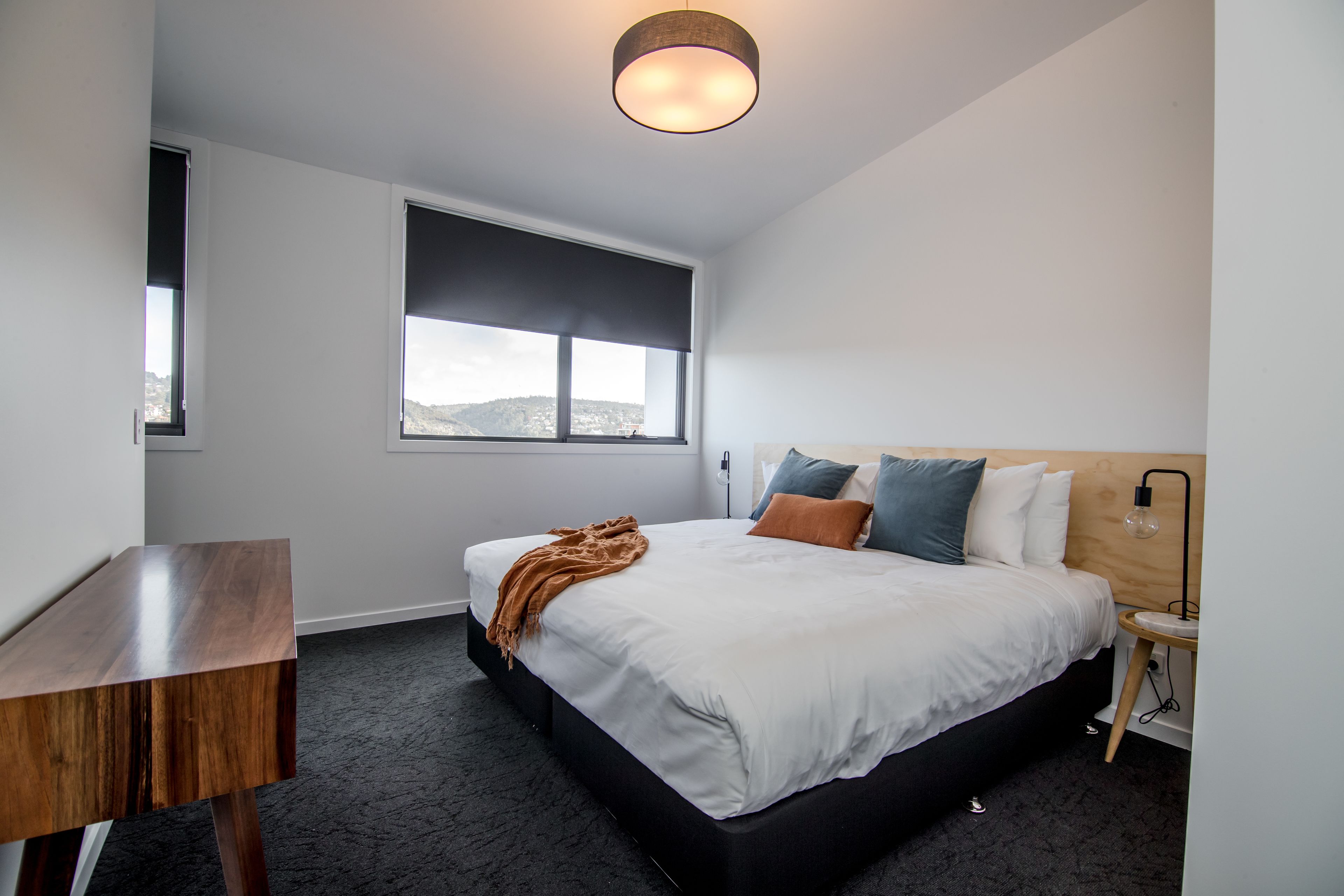 Een moderne hotelkamer met een groot bed, een nachtkastje, een bureau, een raam met uitzicht en een plafondlamp.