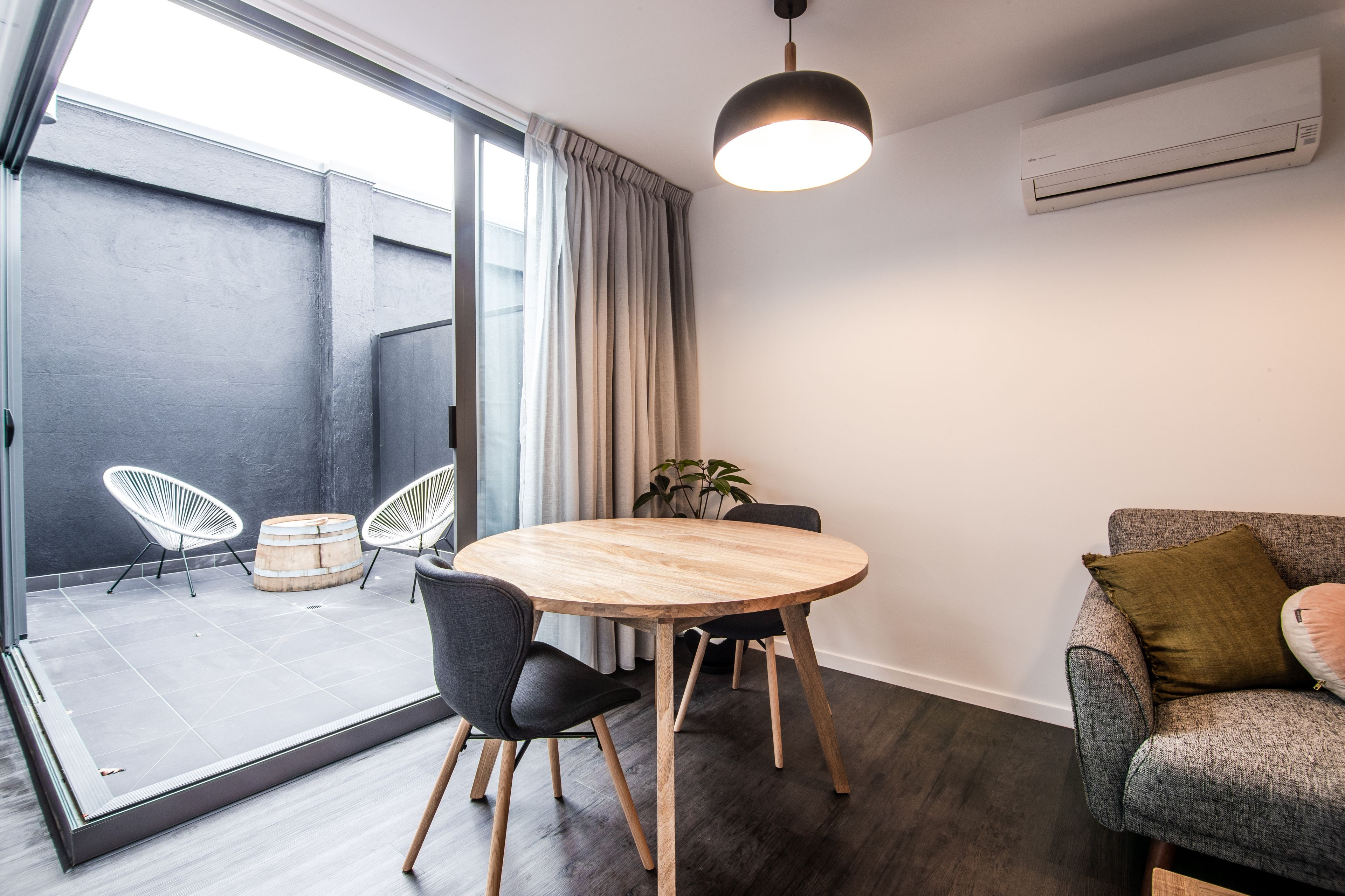 A modern interior with a round wooden table, black chairs, a grey sofa, and a hanging light fixture.