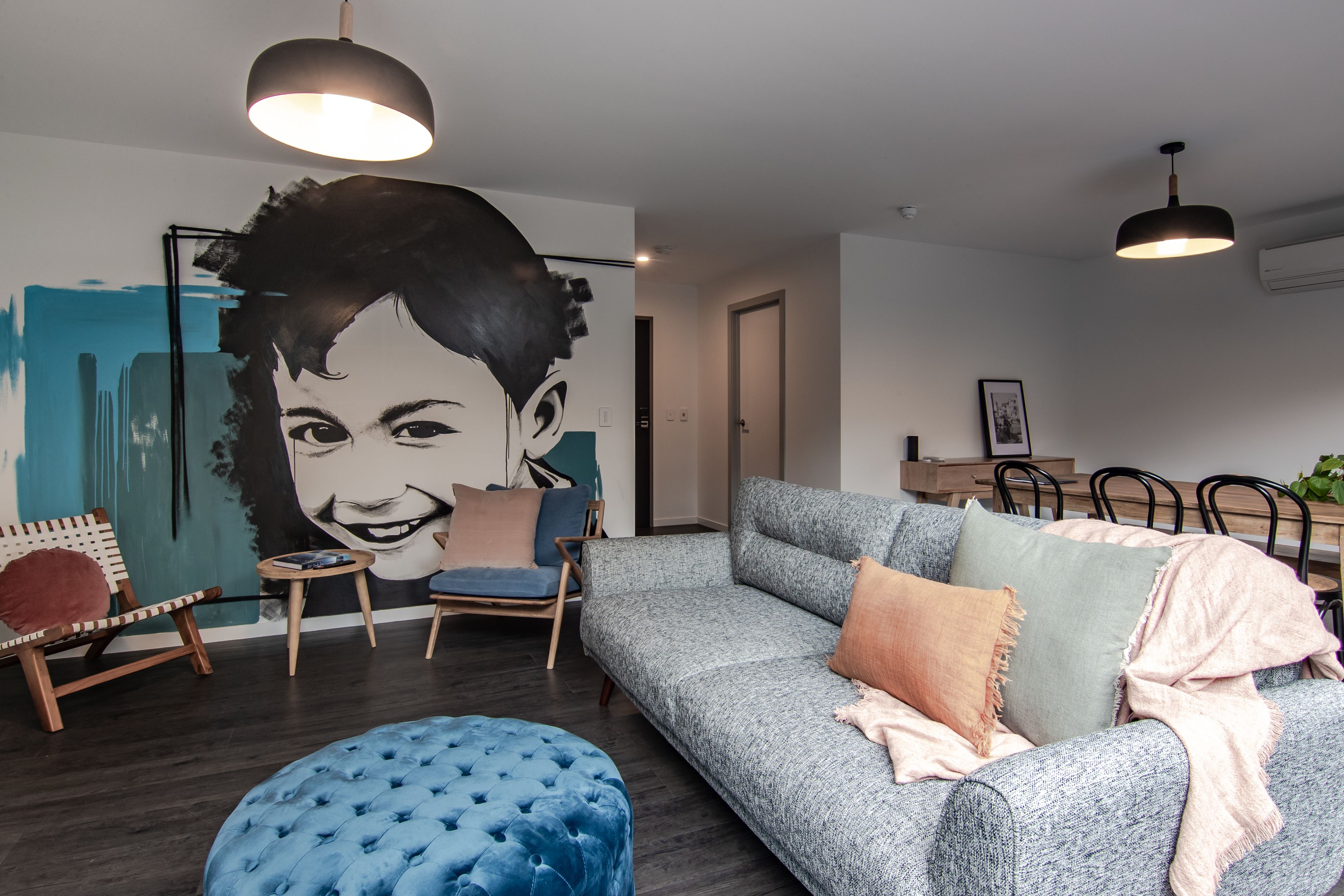 A modern living room with a grey sofa, blue ottoman, and a large wall mural.