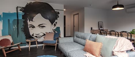 A modern living room with a grey sofa, blue ottoman, and a large wall mural.