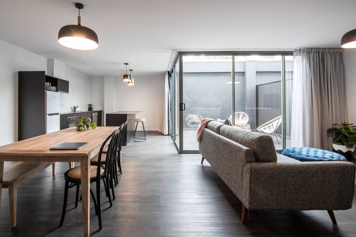 Un espacio habitable moderno con una mesa de comedor de madera, sillas negras, un sofá gris y un reposapiés azul.