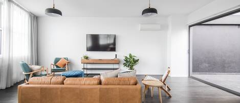 Una sala moderna con un sofá grande, una mesa de centro y un televisor montado en la pared. Hay una puerta corrediza de vidrio que da a un balcón.