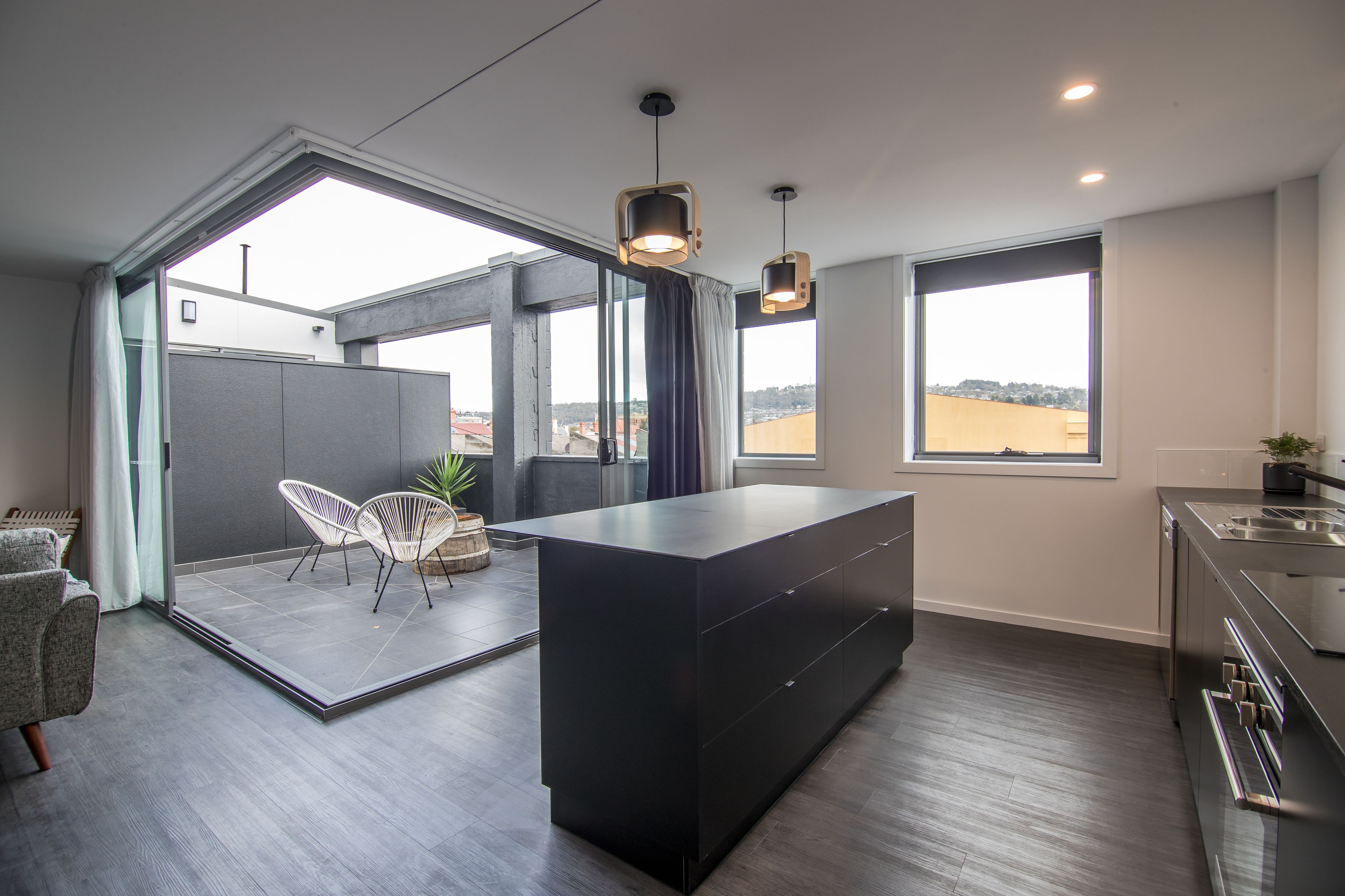 A modern kitchen with a large island, two pendant lights, and a view of the city through large windows.