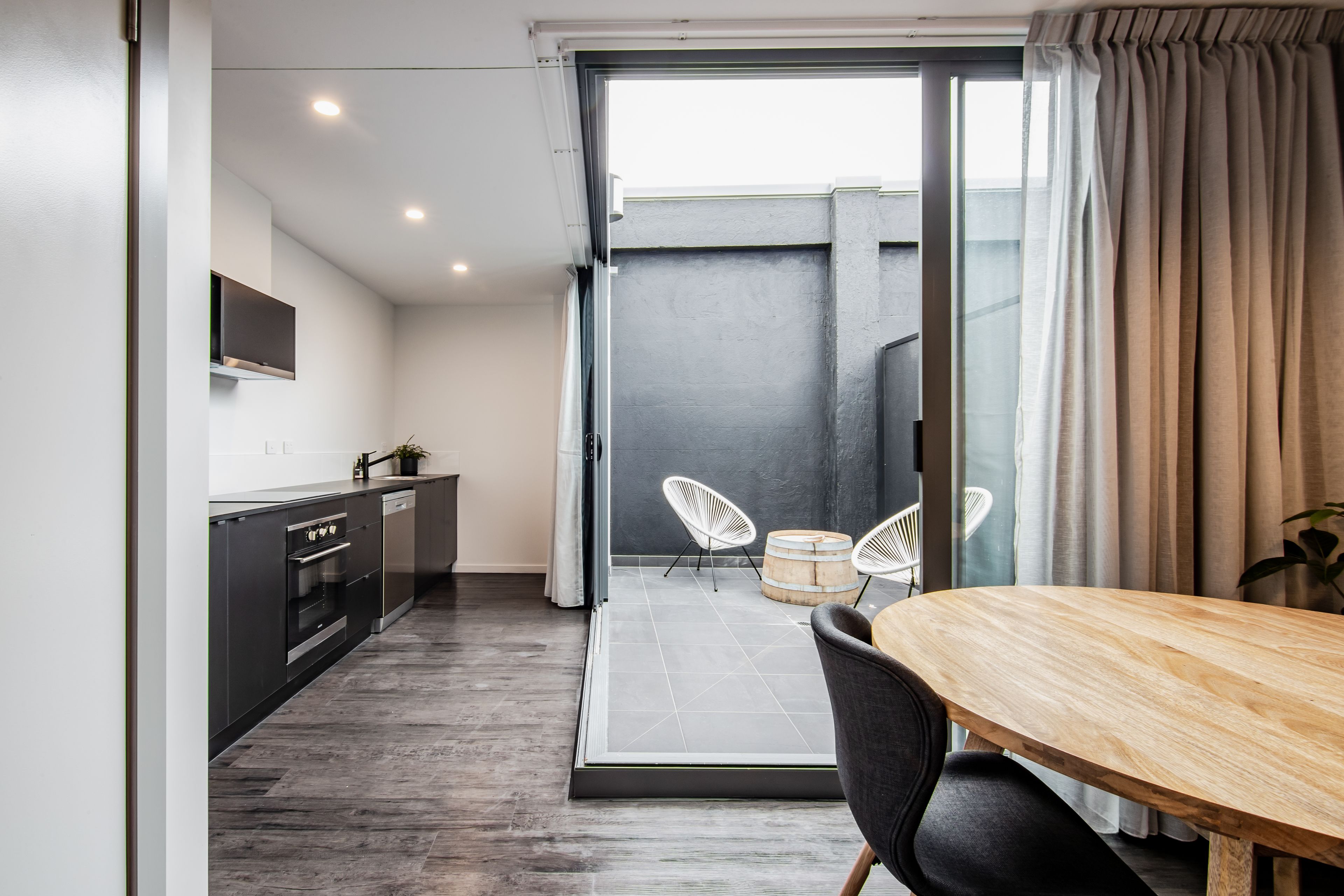 A modern kitchen with dark cabinetry, a wooden dining table, and two white chairs.