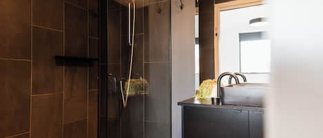 A modern bathroom with a glass-enclosed shower, a dark tiled wall, and a sink with a mirror above it.