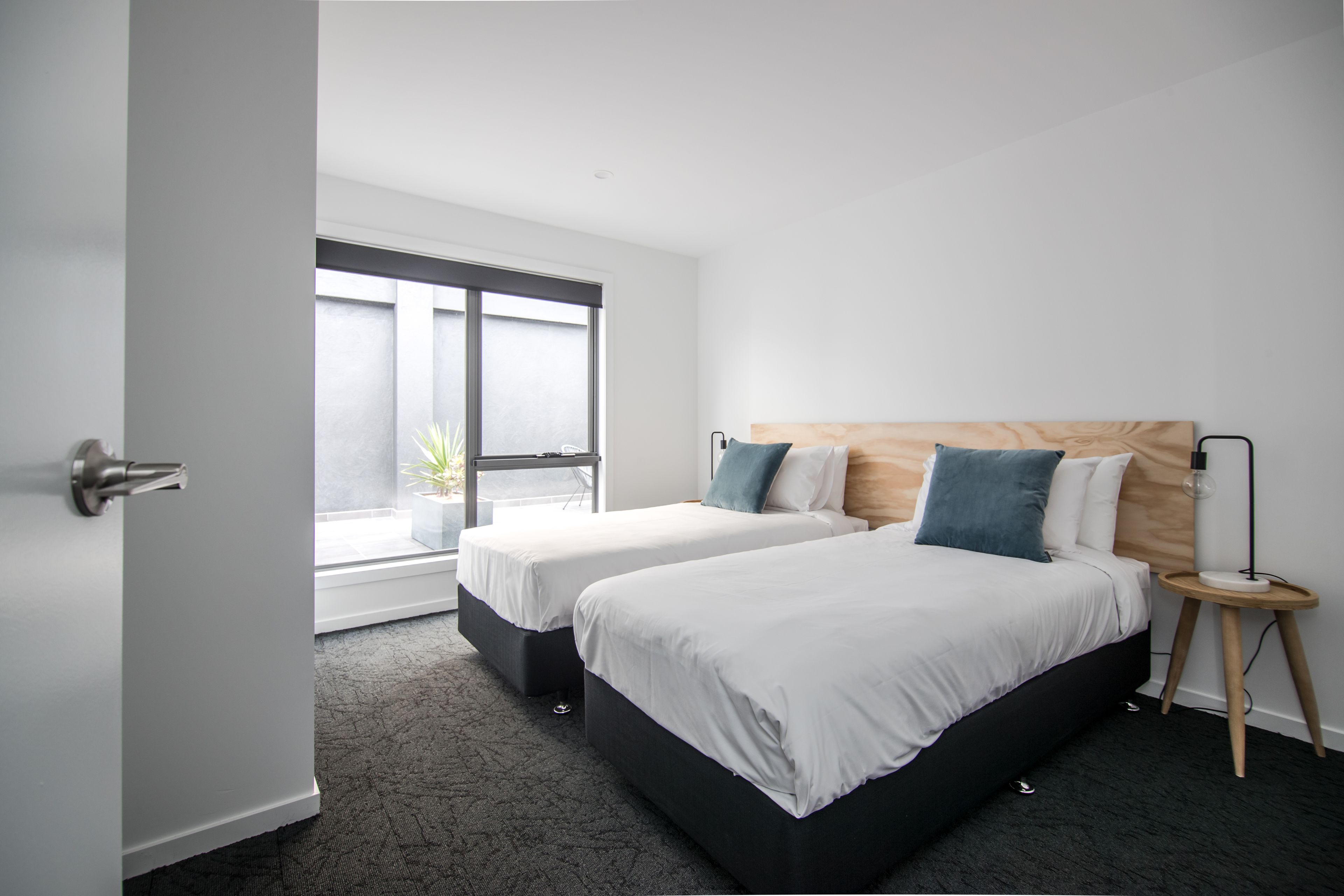 A modern hotel room with two beds, a large window, and a small bedside table.