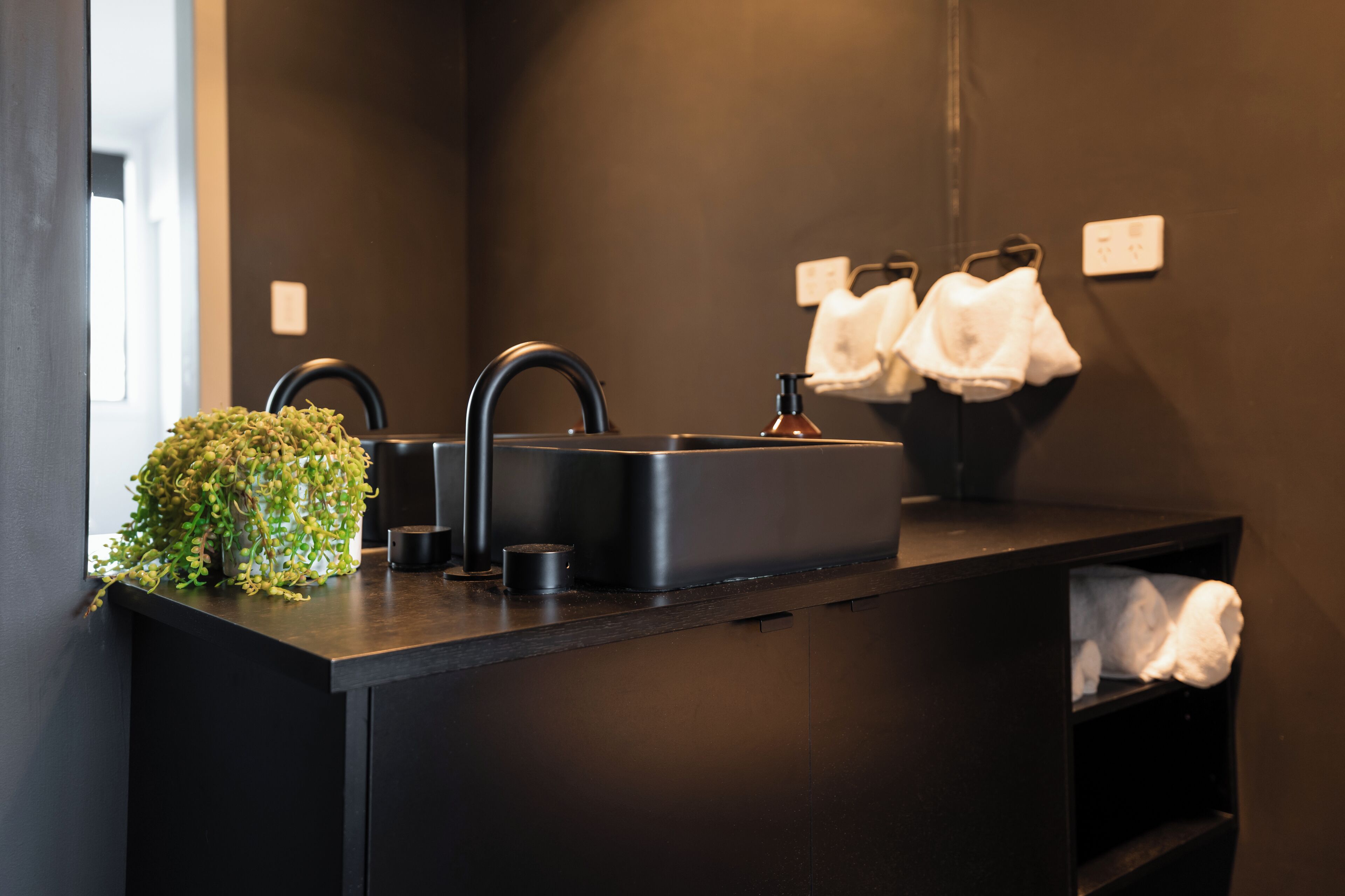 Een moderne badkamer met een zwart wastafel, kraan en een kleine plant op het aanrecht.