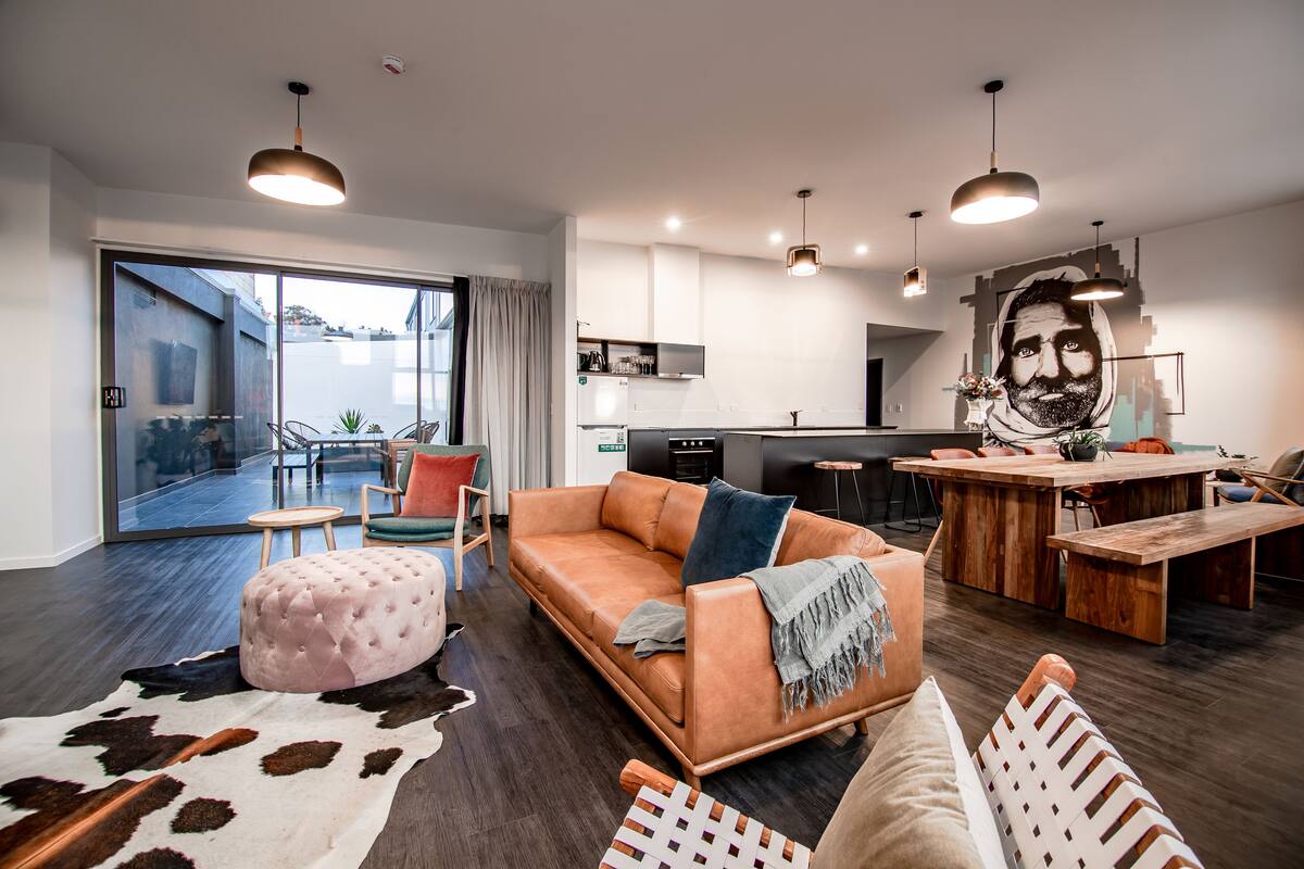 Una sala de estar moderna con un sofá, reposapiés y comedor con mesa de madera.