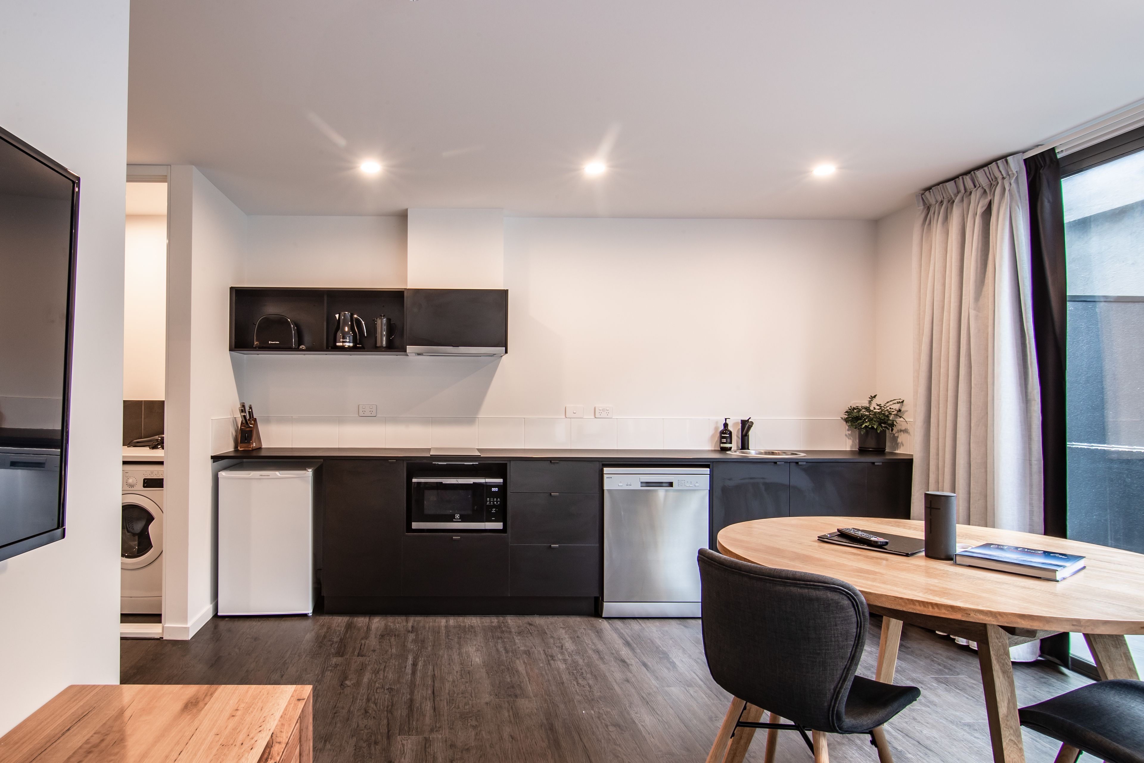 A modern kitchen with built-in appliances, a dining area with a wooden table and chairs, and a large window with curtains.