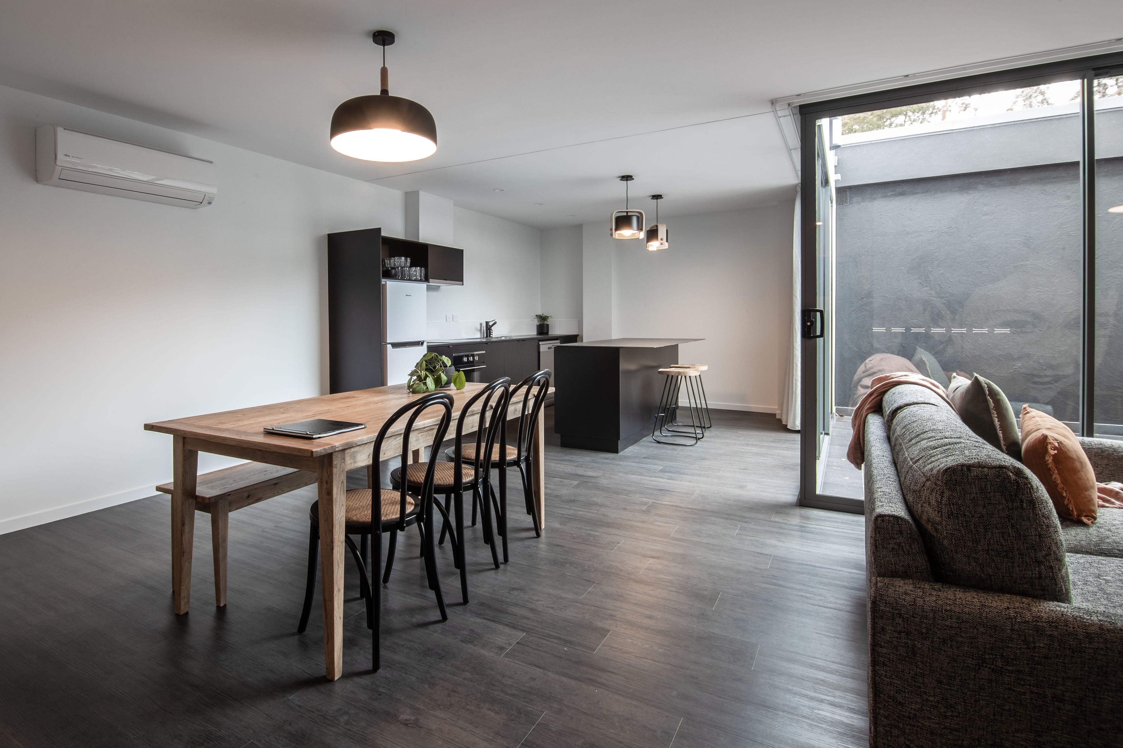 A modern kitchen with a dining area, a sofa, and a sliding glass door leading to a balcony.