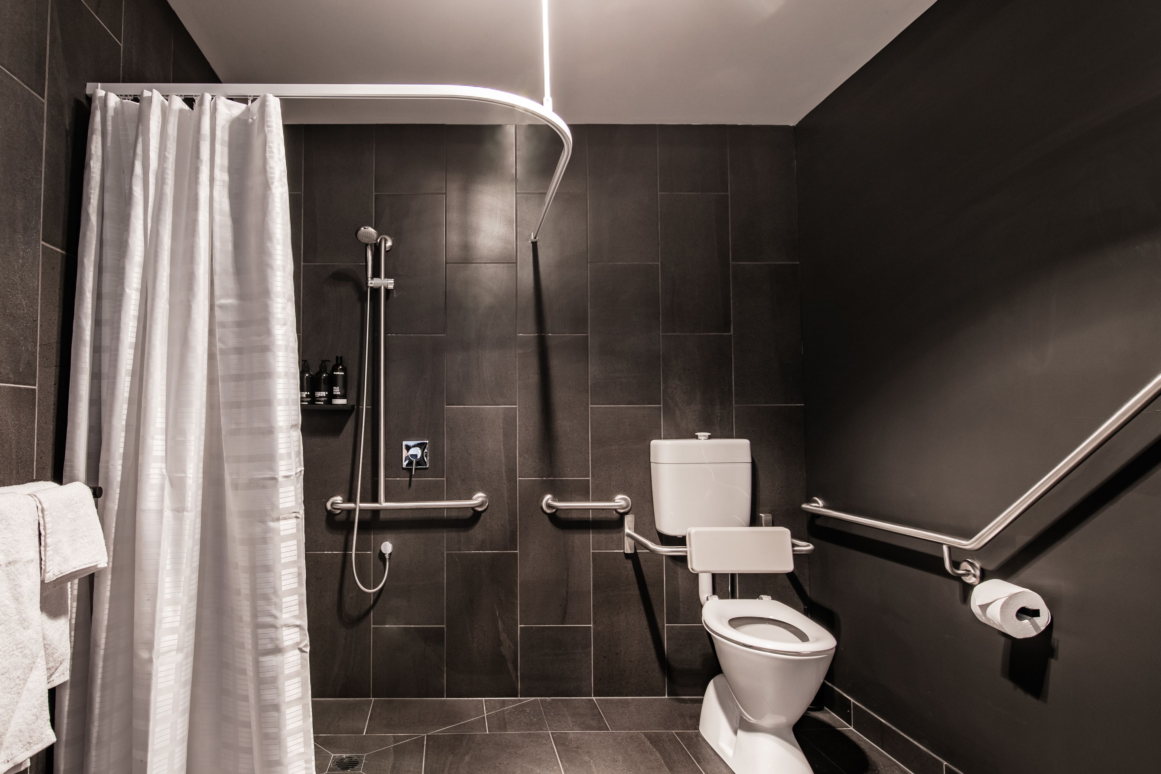 A modern bathroom with a shower, toilet, and grab bars.
