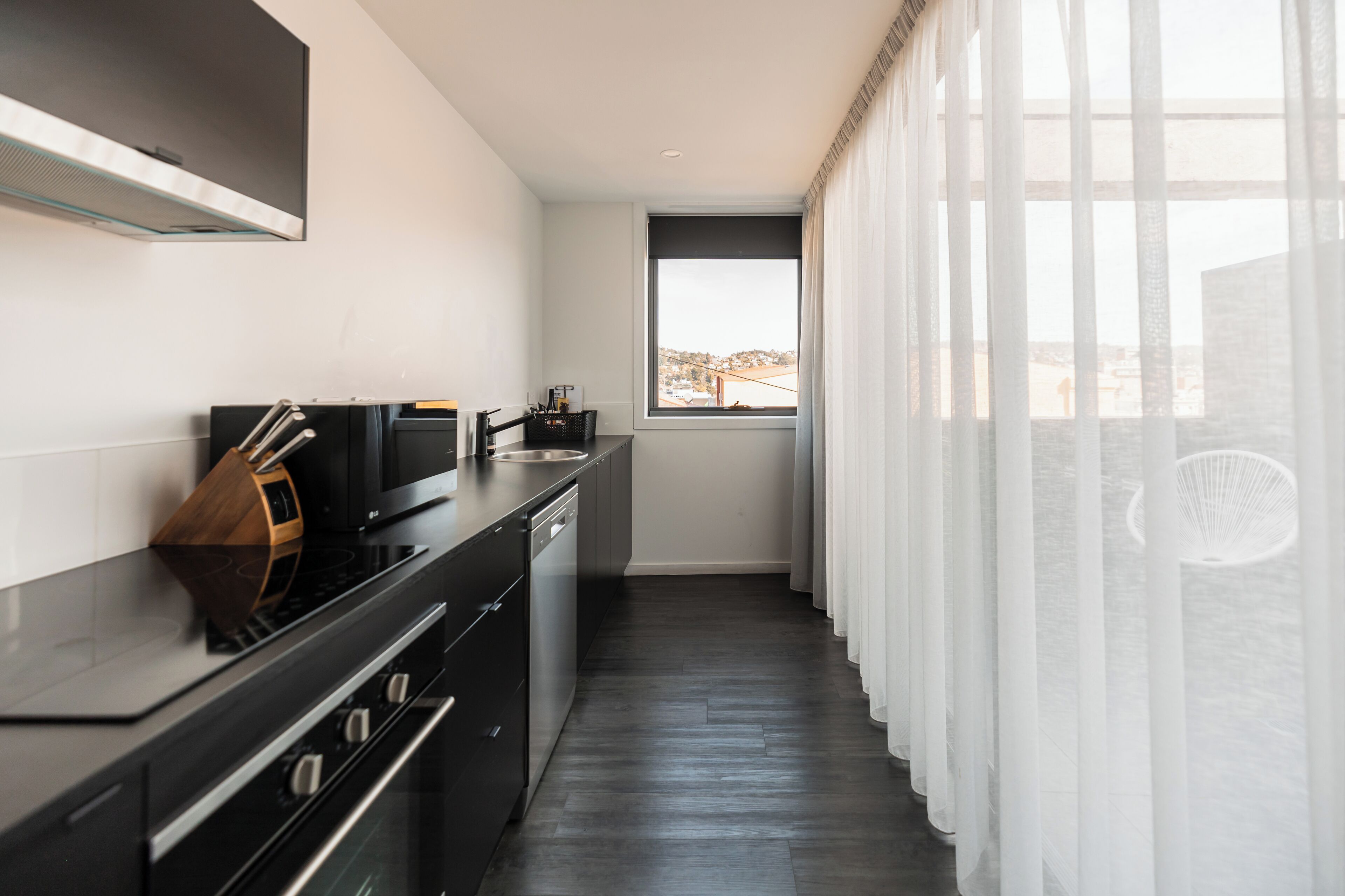 Een moderne keuken met een ingebouwde kookplaat, oven en vaatwasser. Er is een raam met uitzicht op een gebouw.