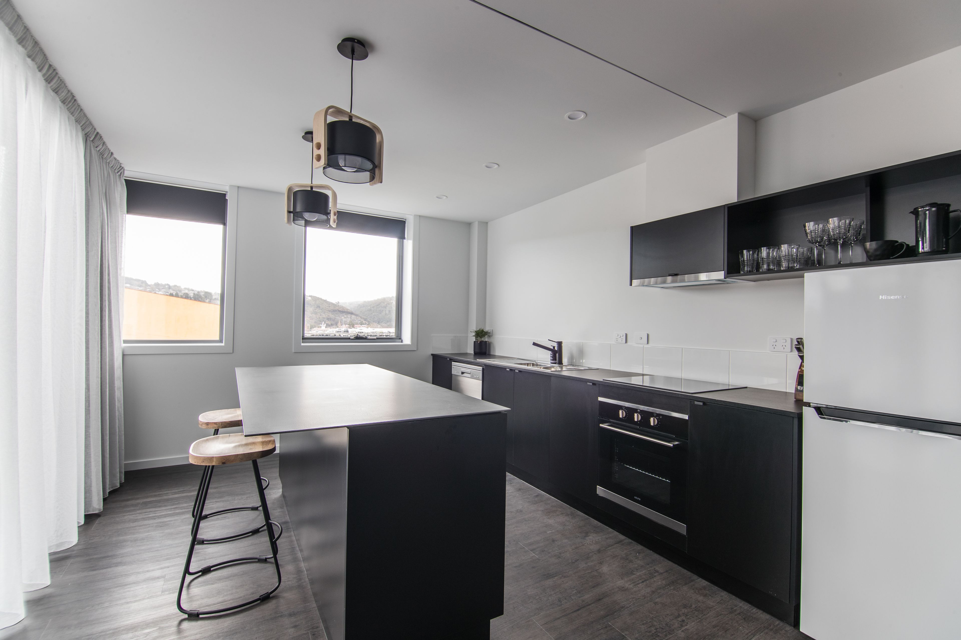 A modern kitchen with a central island, black cabinetry, and a built-in oven.