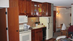 A compact kitchen with wooden cabinets, a white microwave, a coffee maker, and a refrigerator.