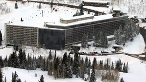 A modern hotel with a long, rectangular building, multiple parking areas, and a ski lift visible in the background.