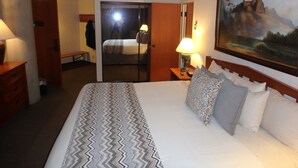 A hotel room with a bed, a painting, a lamp, and a door leading to another room.