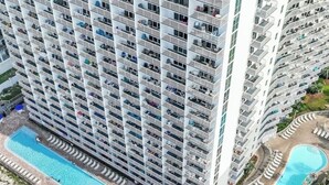 Un hôtel de grande hauteur doté de nombreux balcons, d’une piscine centrale et d’un espace piscine plus petit.