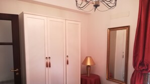 Een slaapkamer met een bed, een kledingkast, een spiegel, een lamp en een klein tafeltje.