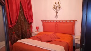 Een slaapkamer met een bed, rode gordijnen, een nachtkastje en een wanddecoratie.