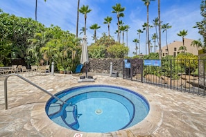 A swimming pool with a stone deck, surrounded by palm trees and a fence.