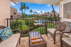 A balcony with wicker furniture, a view of a pool, and a resort building in the background.