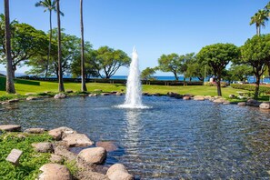 A tranquil fountain surrounded by rocks and greenery, with a clear view of the ocean in the background.