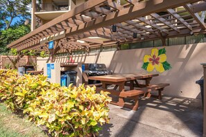 Un espacio de patio exterior con un pergolado de madera, una mesa de picnic y una parrilla.