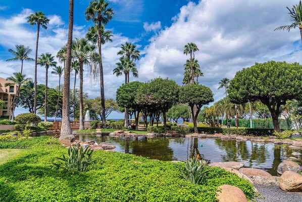 Un jardin aménagé avec des palmiers, un étang et une vue sur une étendue d’eau.
