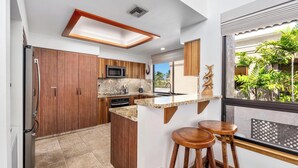 Eine moderne Küche mit Holdekor, einer Granit Arbeitsplatte und einer eingebauten Mikrowelle. Zwei Holzhocker und ein Fenster mit Blick auf Grünflächen.