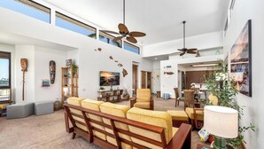 Ein geräumiger Wohnbereich mit hoher Decke, Deckenventilatoren, einem großen Sofa und einem Essbereich mit Stühlen.