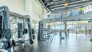 Een ruime fitnessruimte met krachttrainingsapparatuur, een tussenverdieping en grote ramen.