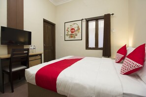 A hotel room with a bed, a desk, a chair, a television, and a window with curtains. - OYO 572 Omah Gedongkuning Syariah Homestay (Yogyakarta)