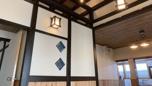 Une pièce avec des poutres apparentes, un mur blanc orné de deux motifs en forme de losange bleus, et un luminaire au plafond.
