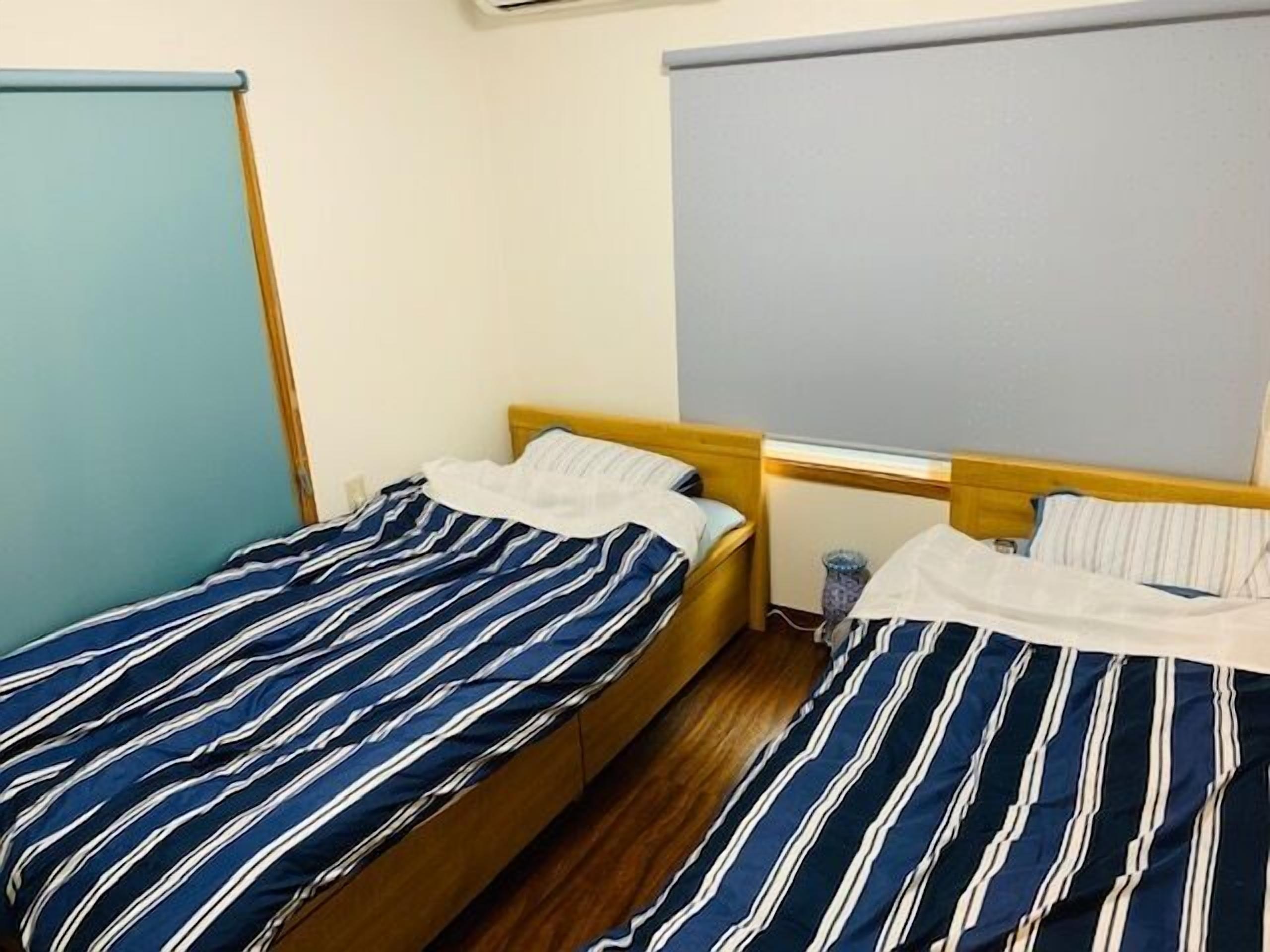A room with two beds, each with striped bedding, wooden headboards, and a small bedside table.
