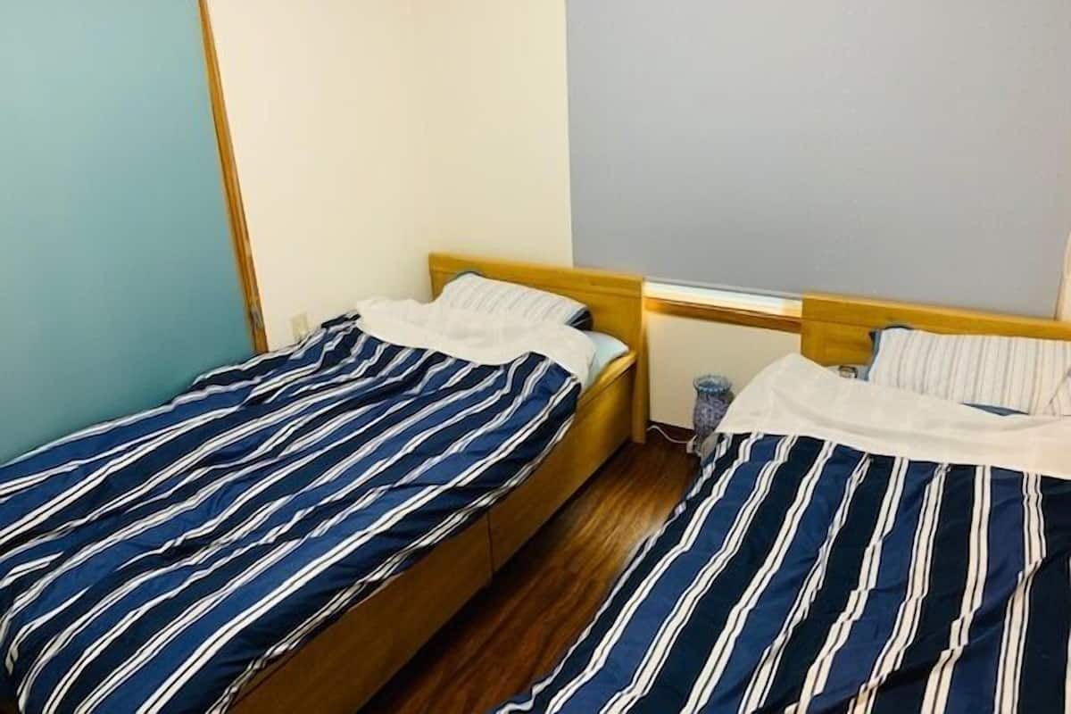 A room with two beds, each with striped bedding, wooden headboards, and a small bedside table.