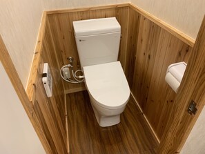 A compact wooden bathroom with a white toilet, a hand dryer, and a paper towel dispenser.