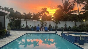 A swimming pool with two lounge chairs and a small table, surrounded by palm trees and potted plants. - BY THE BEACH WITH A POOL! PRIVATE GUEST STUDIO APT. WITH A FULL KITCHEN & BATH! (Naples)