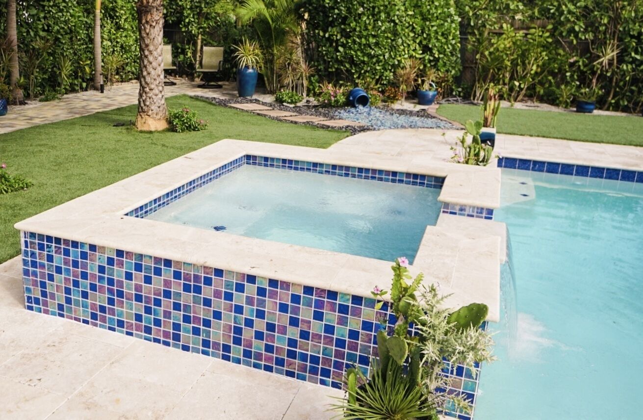 Ein rechteckiger Pool mit blauen Mosaikfliesen und ein umlaufender Garten mit verschiedenen Pflanzen und Bäumen.