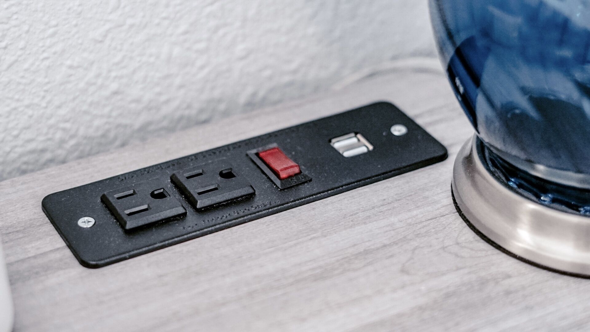 Une prise électrique noire à trois prises, montée sur une surface en bois de couleur claire.