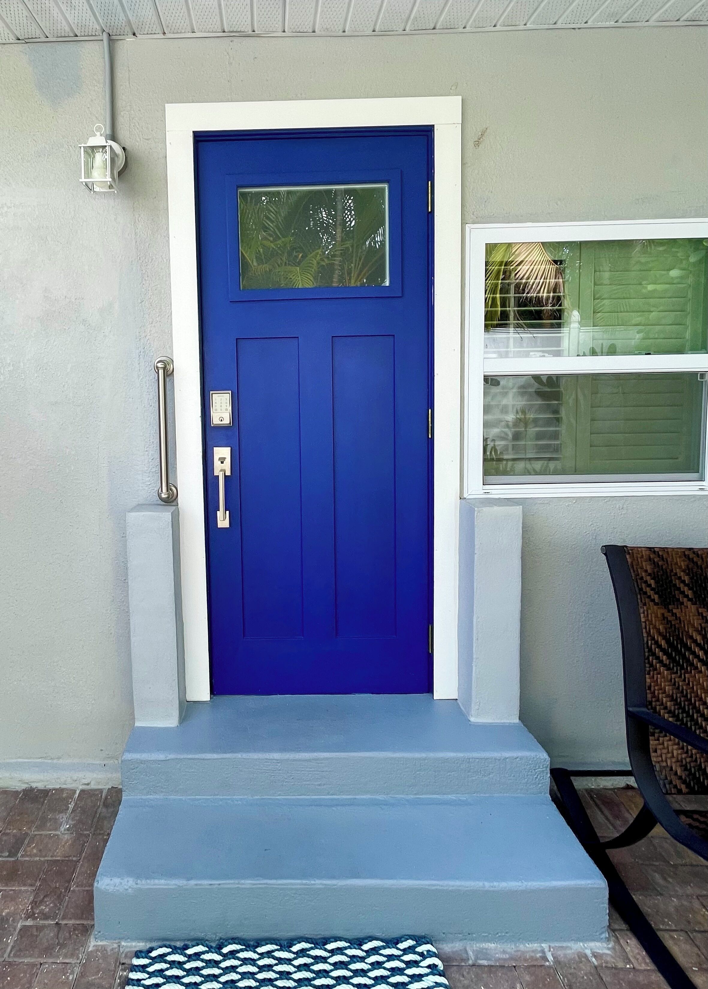 A blue door with a small window above it, a white wall, and a window with blinds to the right.