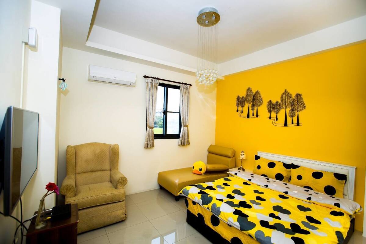 Un dormitorio con cama, dos sillas, un televisor y una ventana con cortinas.