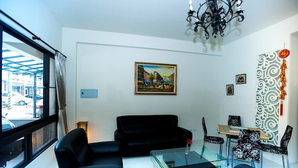 Ein modernes Wohnzimmer mit einer schwarzen Couch, einem Glastisch und einem Essbereich mit gemusterten Stühlen.