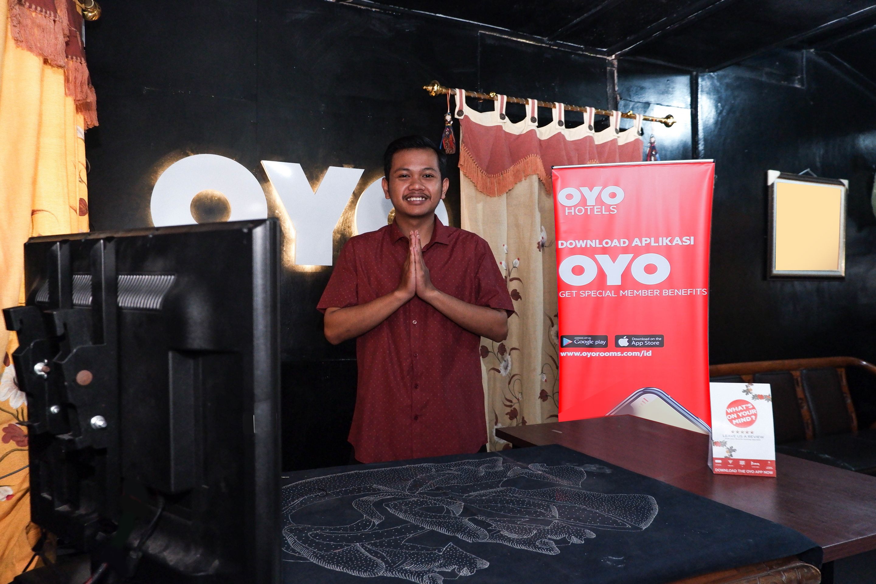A man standing in front of a display with a large 'OYO' sign and a red banner advertising a mobile app.