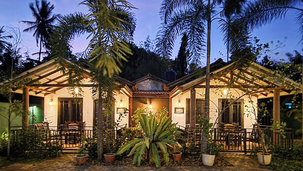 A two-story house with a covered patio, surrounded by palm trees and potted plants. - Max Safari Villa (Udawalawa)