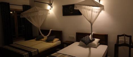 A hotel room with two beds, each with a canopy. There is a small table between the beds, and a chair is placed near the window.